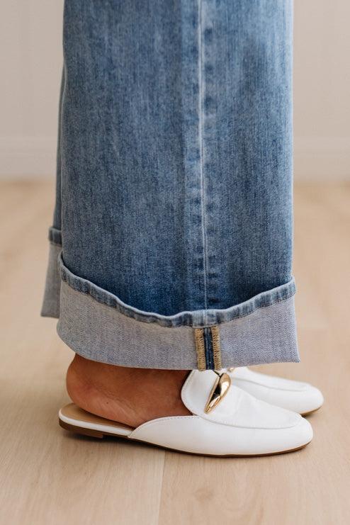 White loafers worn with rolled-up blue jeans on a wooden floor.
