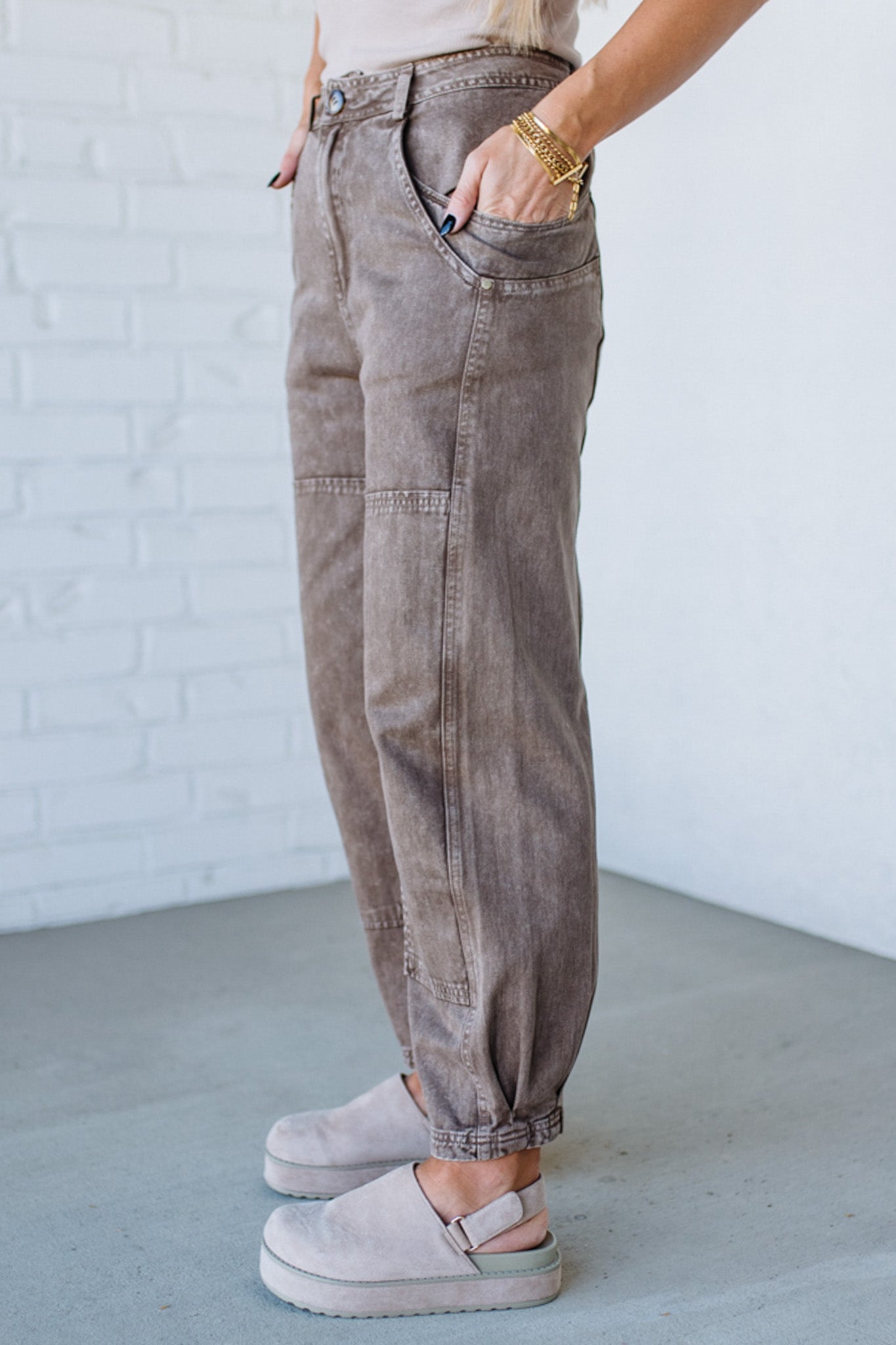 Person wearing beige high-waisted pants and light-colored shoes against a white brick wall.