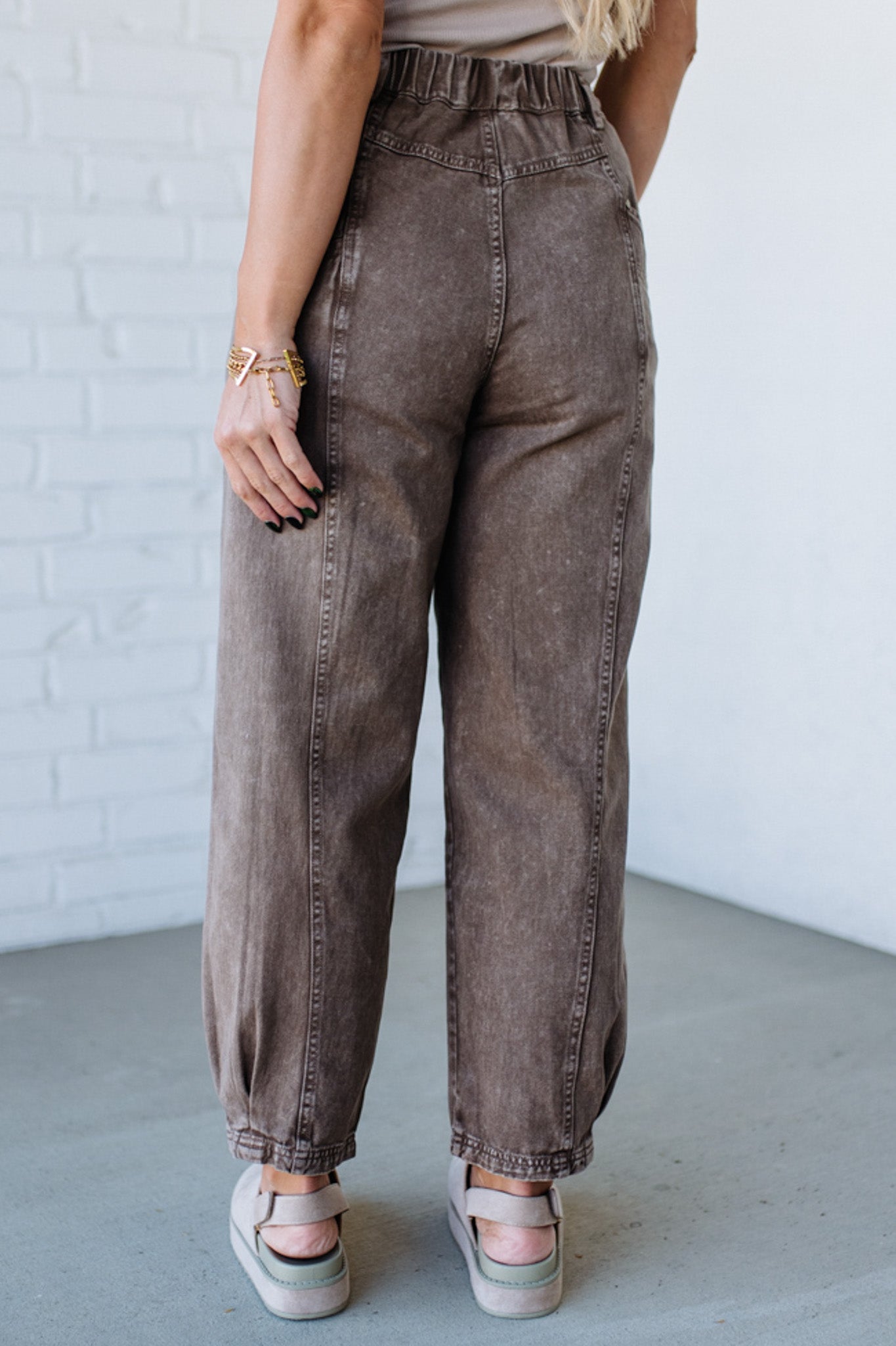 Person wearing brown wide-leg jeans against a white brick wall.