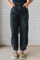 Person wearing black acid-wash jeans and brown shoes against a white brick wall.