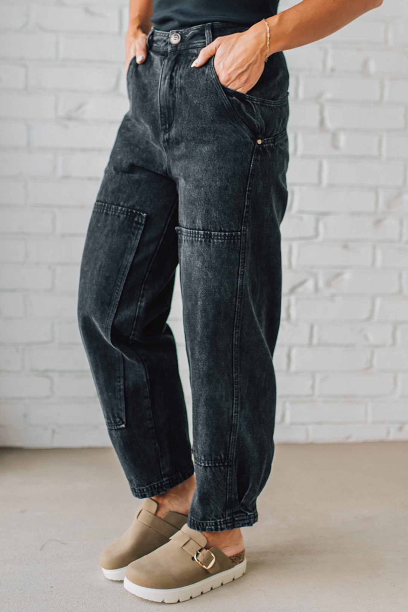 Person wearing dark jeans and brown shoes against a white brick wall.