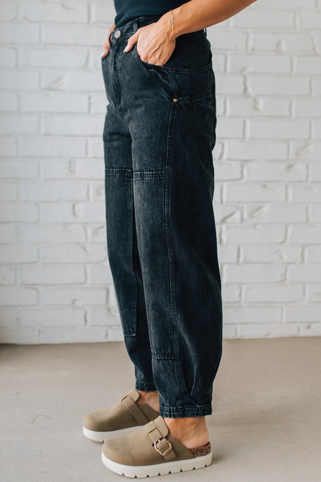 Person wearing dark jeans and brown shoes against a white brick wall.