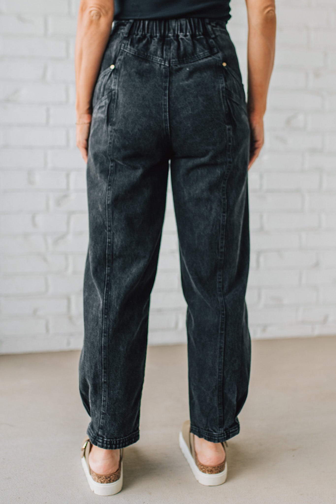 Person wearing black acid-wash jeans against a light brick wall.