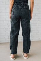 Person wearing black acid-wash jeans against a light brick wall.