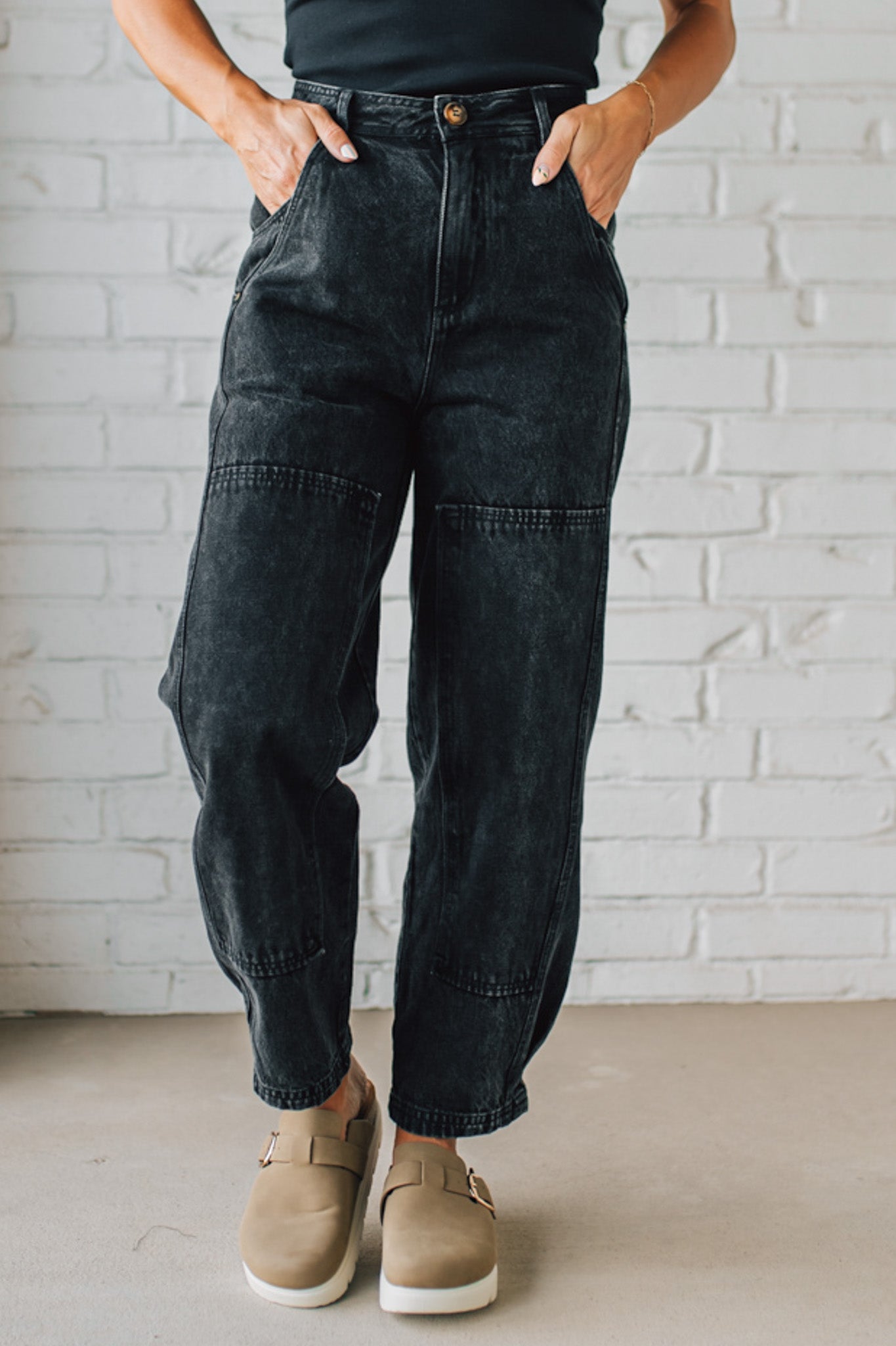 Person wearing black cargo pants with a white brick wall background