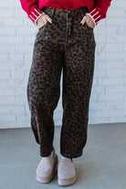 Person wearing leopard print pants with a red sweater against a white brick wall.