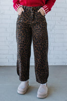 Person wearing leopard print pants and a red sweater against a white brick wall.