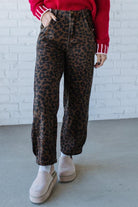 Person wearing leopard print pants and a red sweater against a white brick wall.