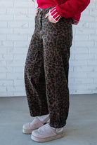 Person wearing leopard print pants with a red sweater and pink shoes against a white brick wall.