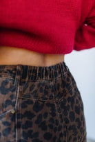 Person wearing a red sweater and leopard print pants against a white background