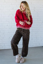 Woman wearing a red sweater and leopard print pants against a white brick wall.