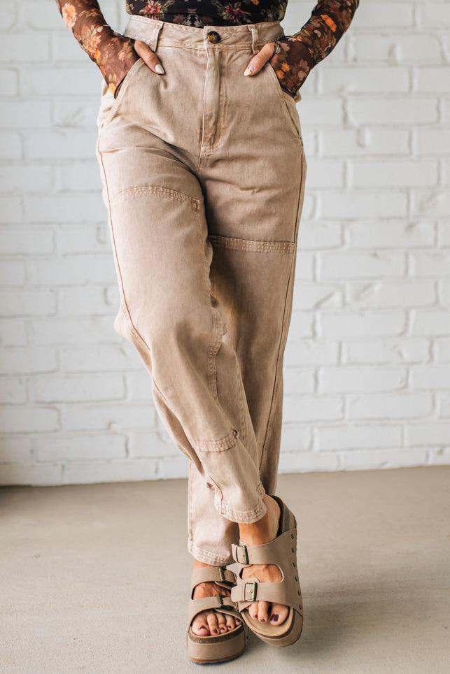 Person wearing beige pants and sandals against a white brick wall.