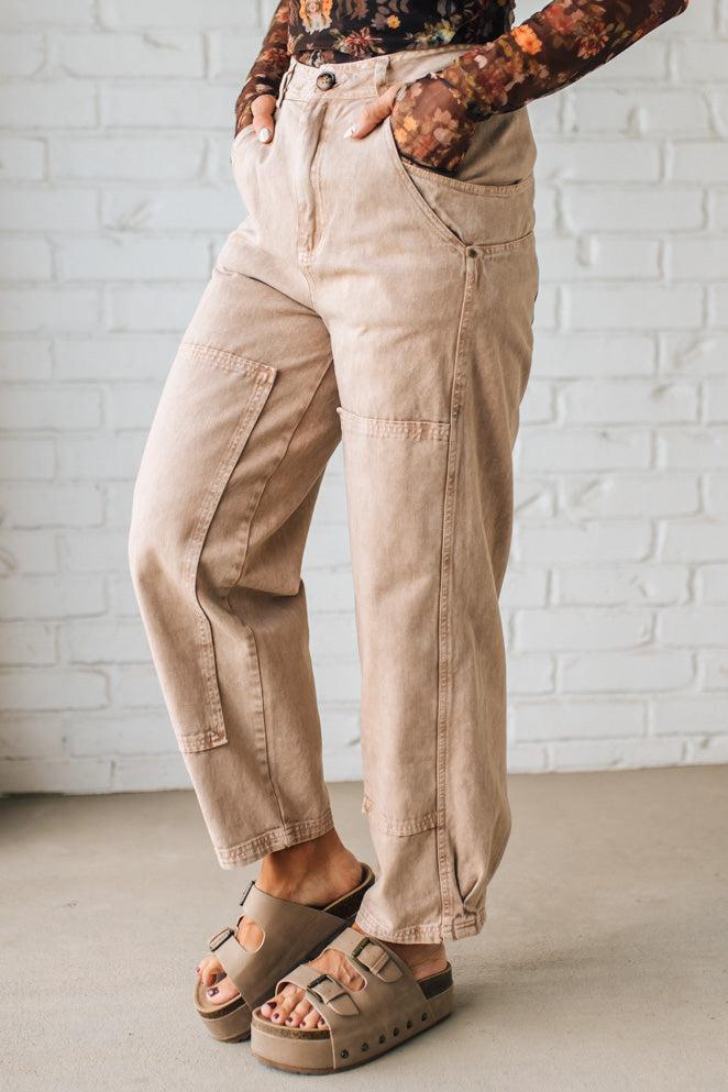 Person wearing beige cargo pants and sandals against a white brick wall.
