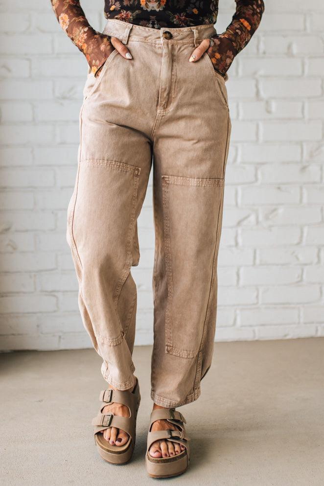 Person wearing beige cargo pants and brown sandals against a white brick wall.