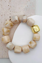Cream bead bracelet with a gold accent bead shown on a textured surface.