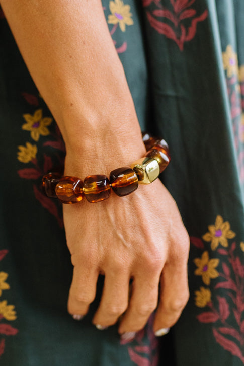 Amber bead bracelet with a gold accent bead shown on a woman's wrist by her side.