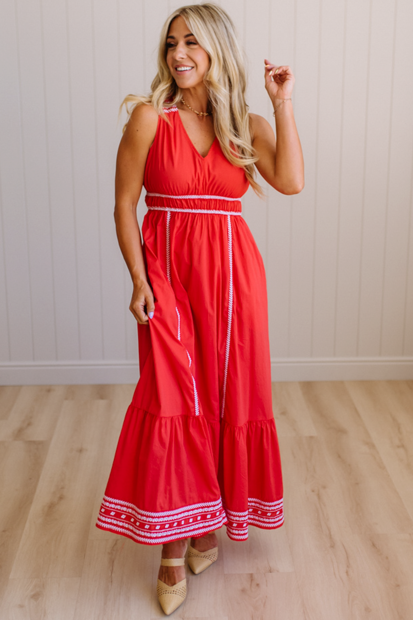 Woman wearing a red dress with white trim in a room with wooden flooring and a white wall.