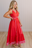 Woman wearing a red dress with white trim in a room with wooden flooring and a light-colored wall.
