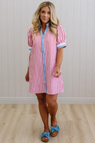 Woman wearing a red and white striped dress with blue trim against a white paneled wall.