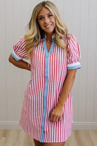 Woman wearing a red and white striped dress with blue trim against a plain background