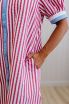 Person wearing a red and white striped dress with blue trim on a plain background