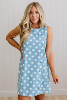 Woman wearing a light blue dress with white polka dots against a white wall.