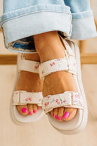 Close-up of feet wearing floral sandals with rolled-up jeans.