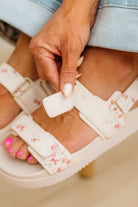 Close-up of a person wearing white floral sandals with a neutral background