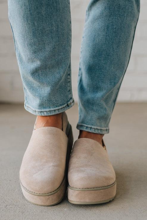 Women's beige sandals worn with blue jeans on a neutral background