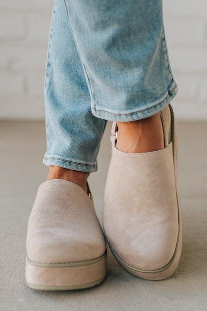 Women's beige sandals worn with blue jeans on a neutral background