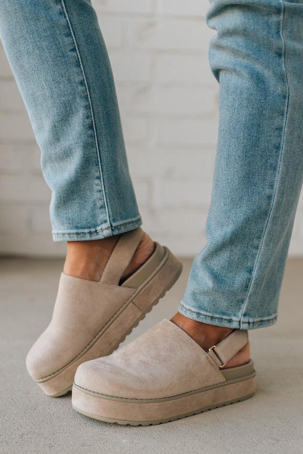 Women's beige sandals worn with blue jeans on a neutral background