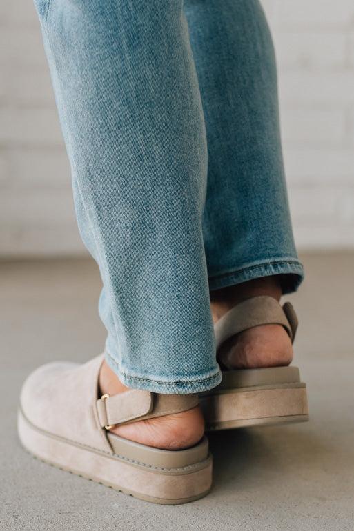 Women's beige sandals worn with blue jeans on a neutral background