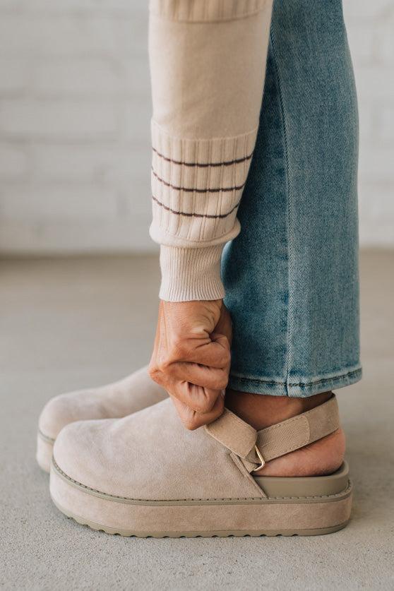Women's beige sandals worn with blue jeans on a neutral background