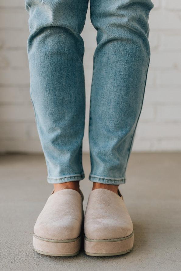 Women's beige sandals worn with blue jeans on a neutral background