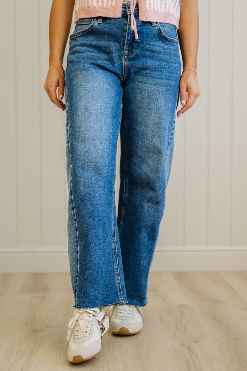 Person wearing blue jeans and white sneakers on a wooden floor with a neutral wall background