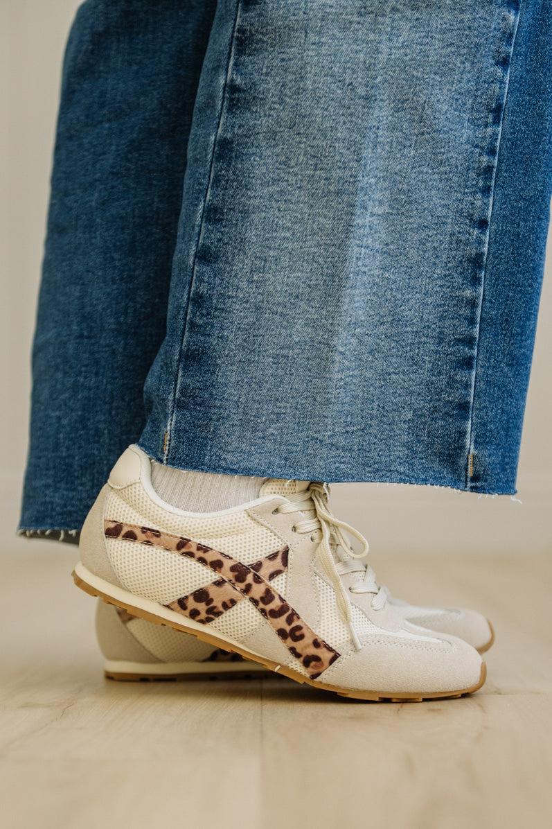 White sneakers with leopard print accents worn with blue jeans on a neutral background