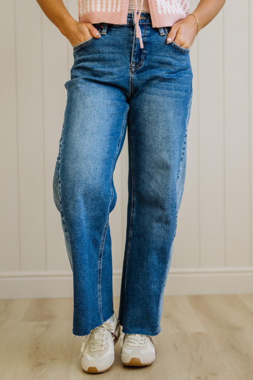 Person wearing blue jeans and white sneakers in a room with a wooden floor and white wall.