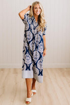 A woman modeling a navy blue and white paisley print midi dress with a striped hem, standing in a room with light wood floors and white paneled walls.