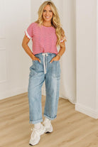 Woman wearing a pink top and blue jeans standing in a room with wooden flooring and white walls.