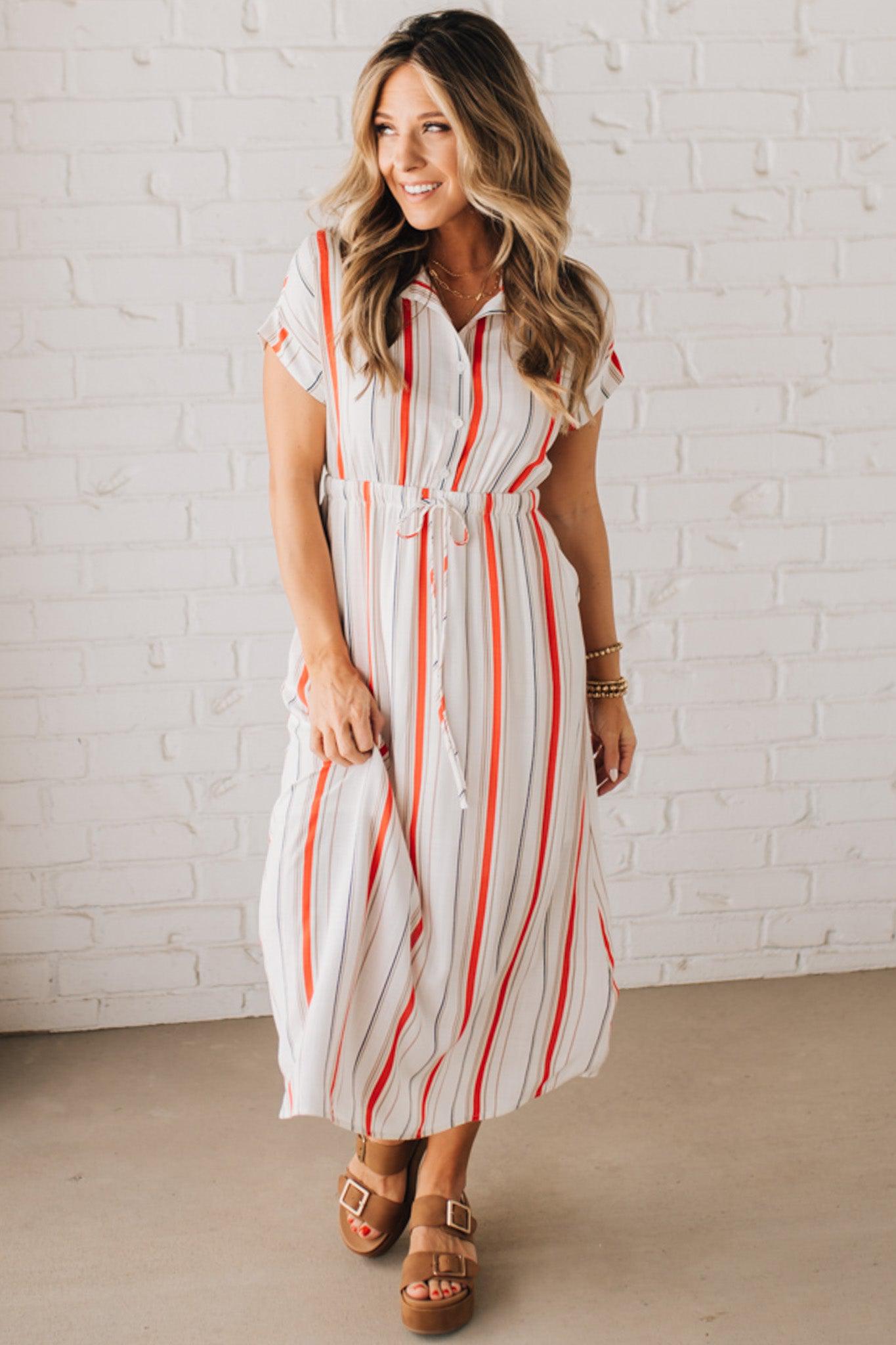 BLONDE WOMAN WEARING A RED AND WHITE DRESS WITH VERTICAL STRIPES, SIDE POCKETS, SHORT SLEEVE, BUTTON DOWN, FAUX TIE WAIST AND MIDI LENGTH.