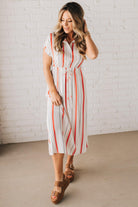 BLONDE WOMAN WEARING A RED AND WHITE DRESS WITH VERTICAL STRIPES, SIDE POCKETS, SHORT SLEEVE, BUTTON DOWN, FAUX TIE WAIST AND MIDI LENGTH.