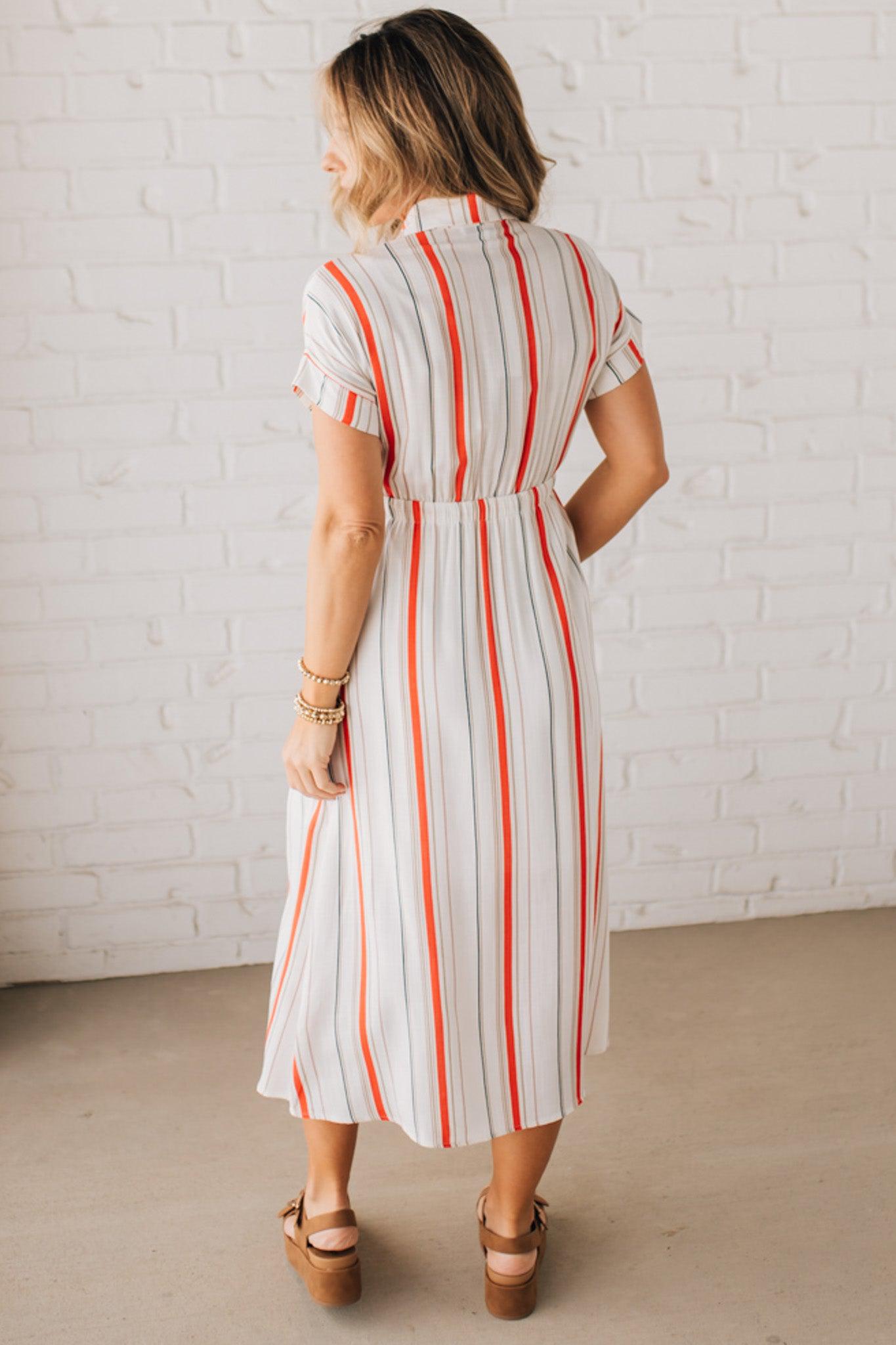 BLONDE WOMAN WEARING A RED AND WHITE DRESS WITH VERTICAL STRIPES, SIDE POCKETS, SHORT SLEEVE, BUTTON DOWN, FAUX TIE WAIST AND MIDI LENGTH.