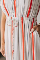 BLONDE WOMAN WEARING A RED AND WHITE DRESS WITH VERTICAL STRIPES, SIDE POCKETS, SHORT SLEEVE, BUTTON DOWN, FAUX TIE WAIST AND MIDI LENGTH.