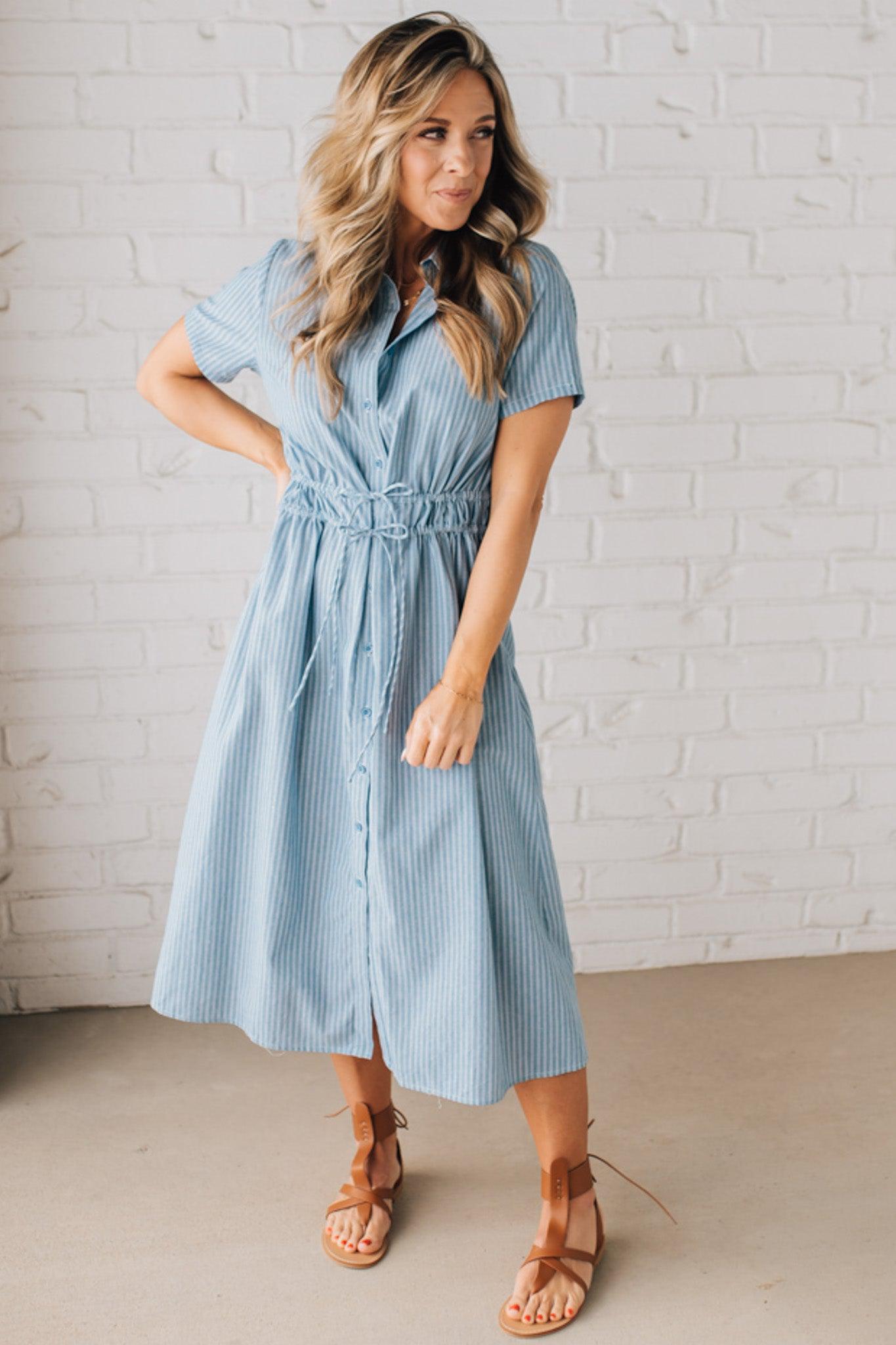 Blonde woman wearing a blue mid lenght dress with button front, double drawstring waist, and collar.