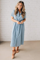 Blonde woman wearing a blue mid lenght dress with button front, double drawstring waist, and collar.