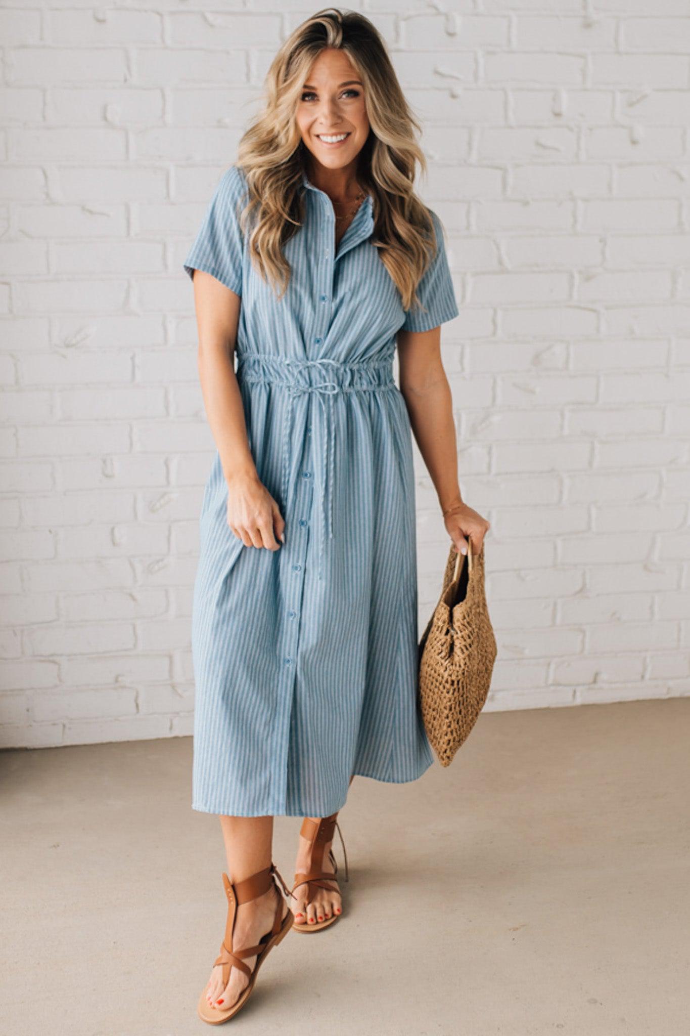 Blonde woman wearing a blue mid lenght dress with button front, double drawstring waist, and collar.