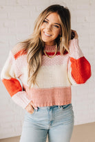 Blonde woman wearing a chunky waist length sweater with pink, mocha, red and cream colors.