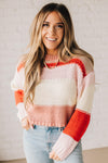 Blonde woman wearing a chunky waist length sweater with pink, mocha, red and cream colors.