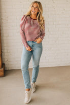 Woman wearing a striped sweater and jeans standing against a white brick wall.