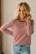 Woman wearing a red and white striped long-sleeve shirt and blue jeans against a white brick wall.